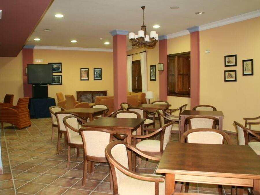 Un comedor con varias mesas y sillas de madera, un televisor sobre un mueble bajo, y cuadros en las paredes.
