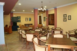 Un espace repas comprenant plusieurs tables et chaises en bois, un téléviseur posé sur un meuble et des tableaux encadrés accrochés aux murs.