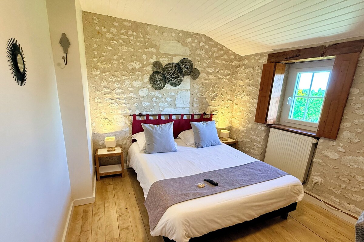 A bedroom with a stone wall, a bed with white bedding, a wooden floor, and a window with a view.