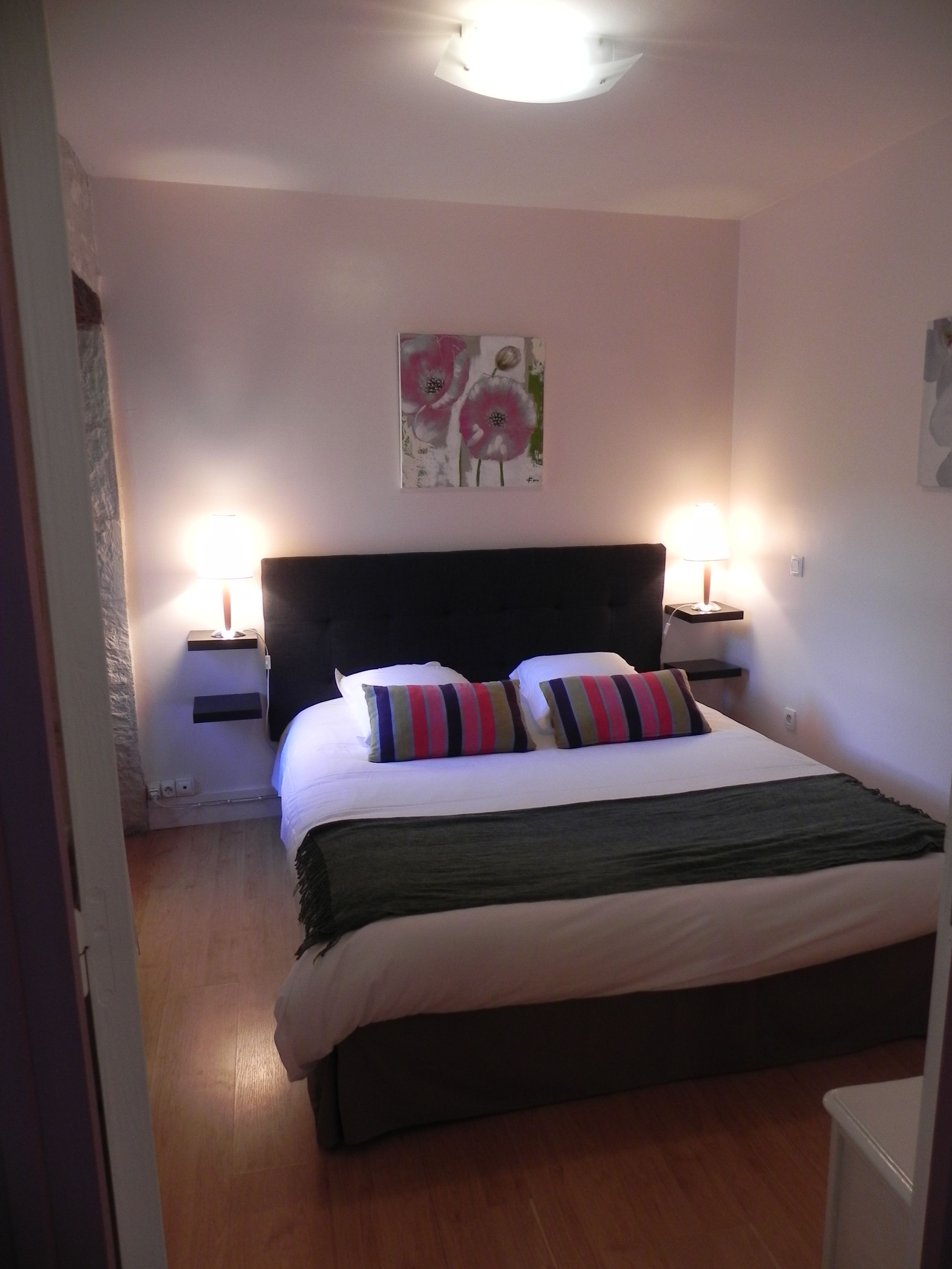 Un dormitorio con una cama, dos lámparas de noche, un cuadro en la pared y suelo de madera.