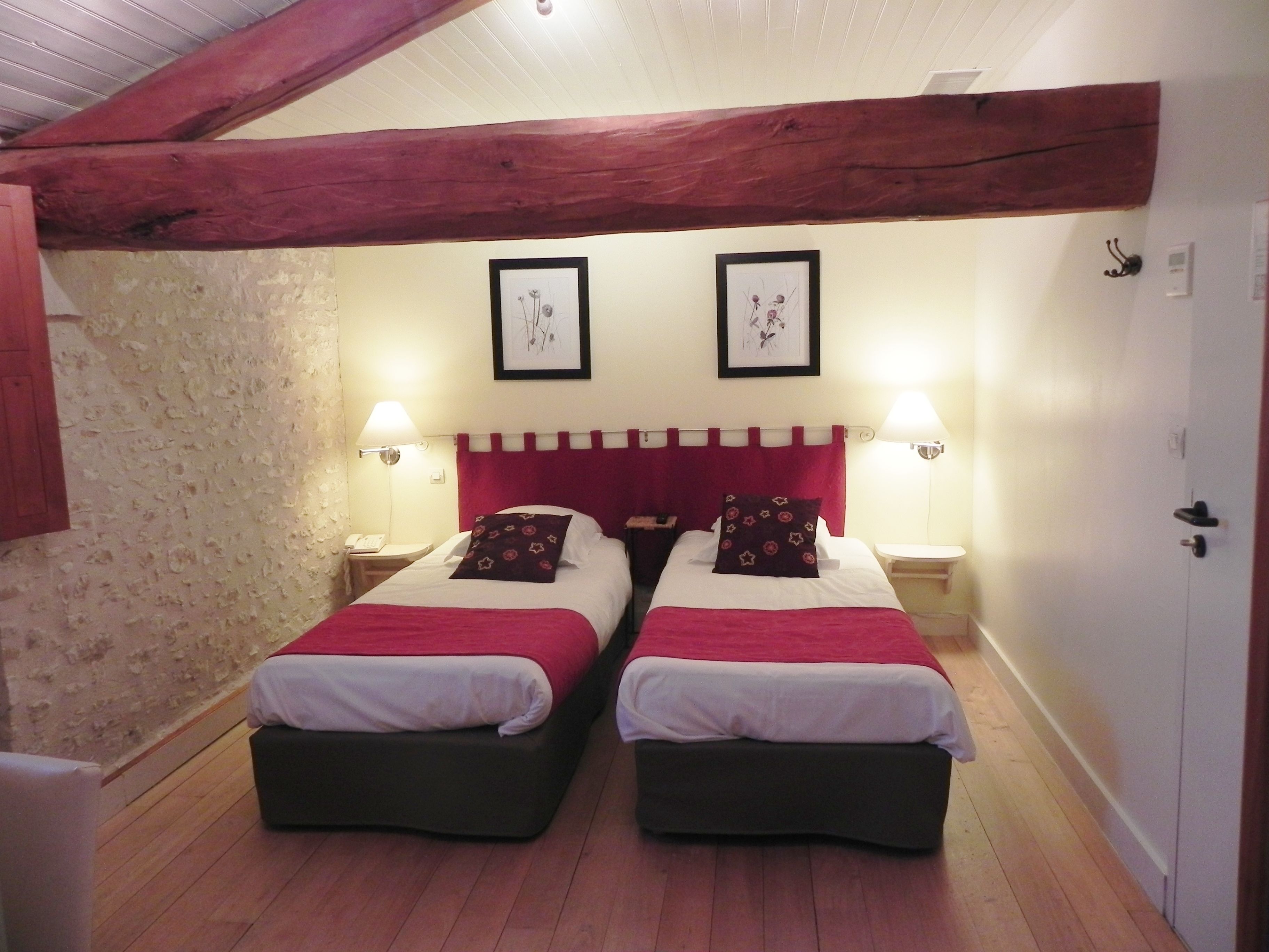 A room with two beds, wooden beams on the ceiling, two framed pictures on the wall, and bedside lamps.