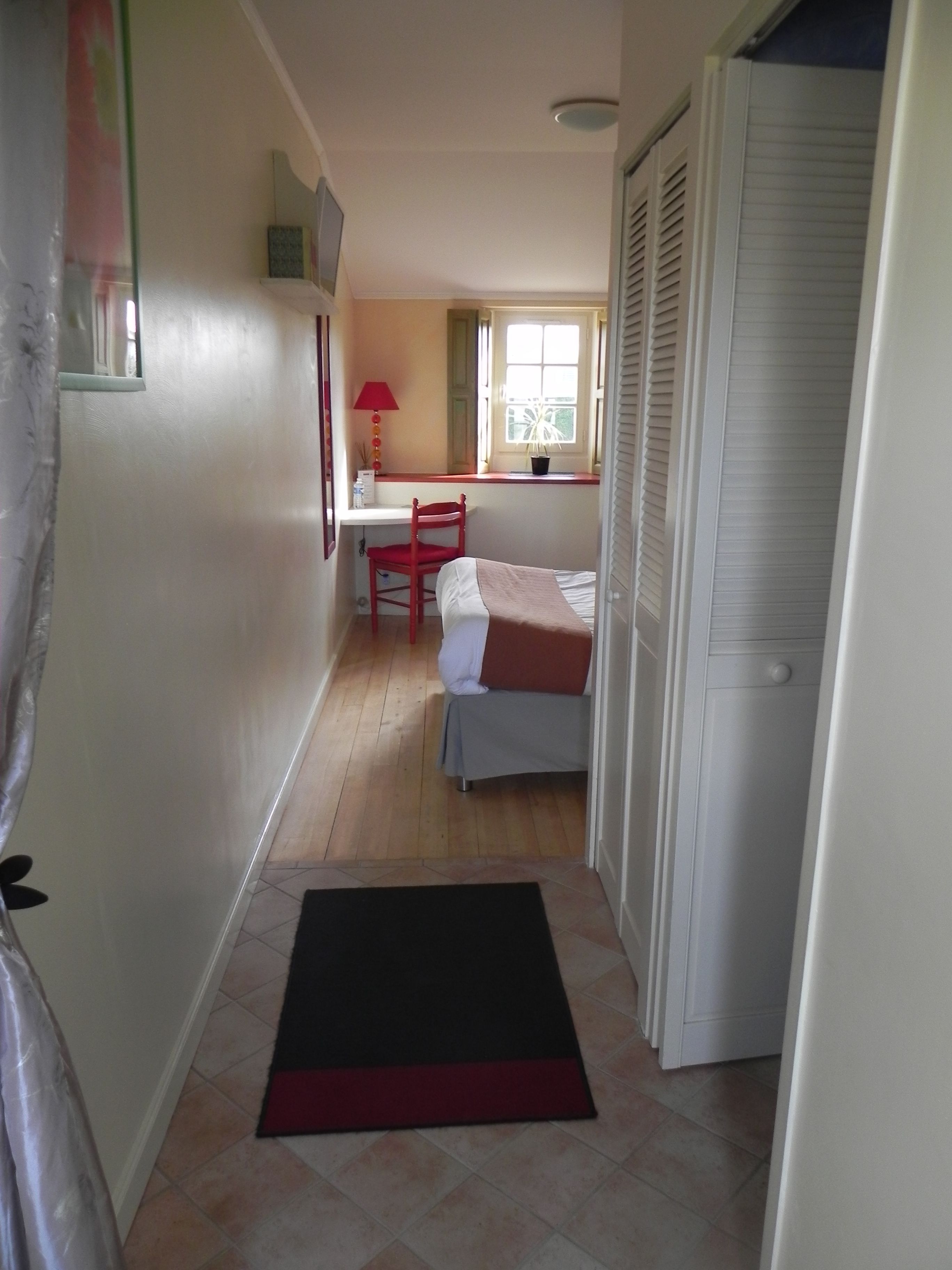 Ein schmaler Flur, der zu einem Schlafzimmer mit einem Bett, einem Schreibtisch und einem Sessel führt.