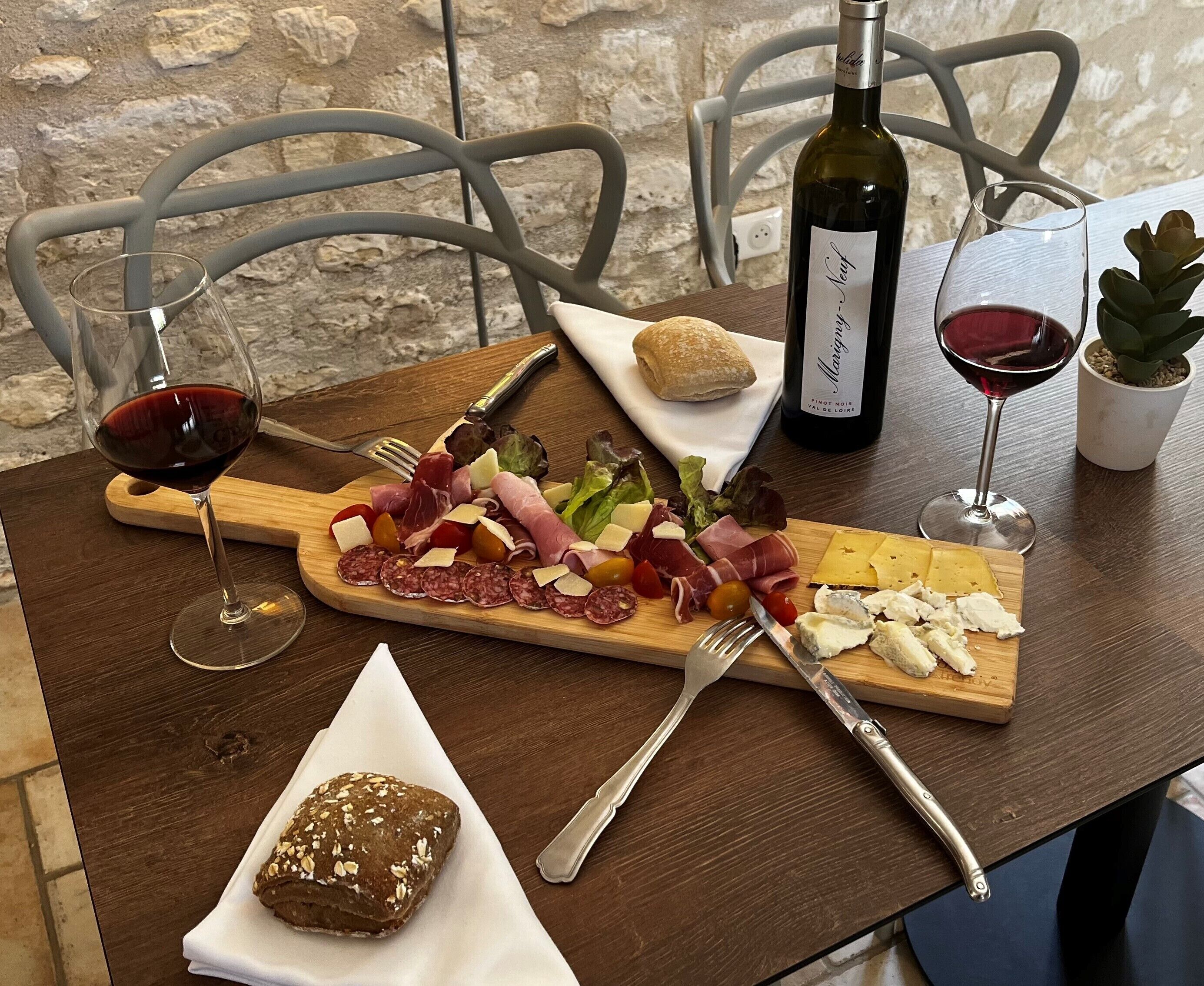 Una mesa de madera con una tabla de embutidos, copas de vino y una botella.