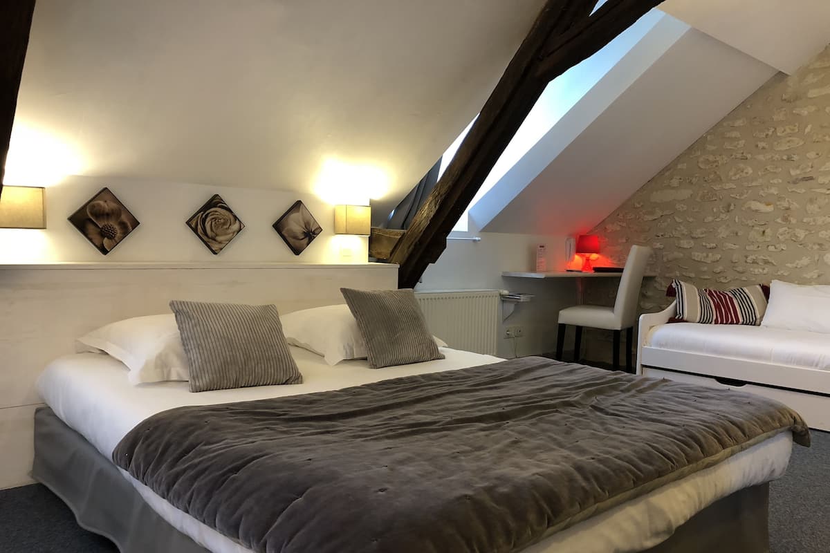 Un dormitorio con una cama grande, un sofá blanco, un escritorio con una silla y un tragaluz.