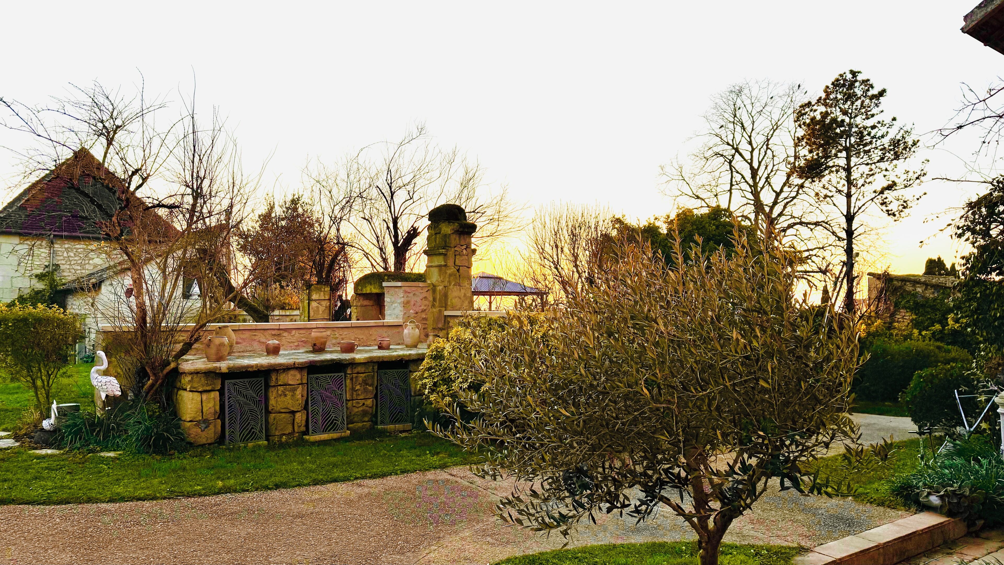 A stone building with a tiled roof, surrounded by a well-maintained garden with a variety of plants and a small tree.
