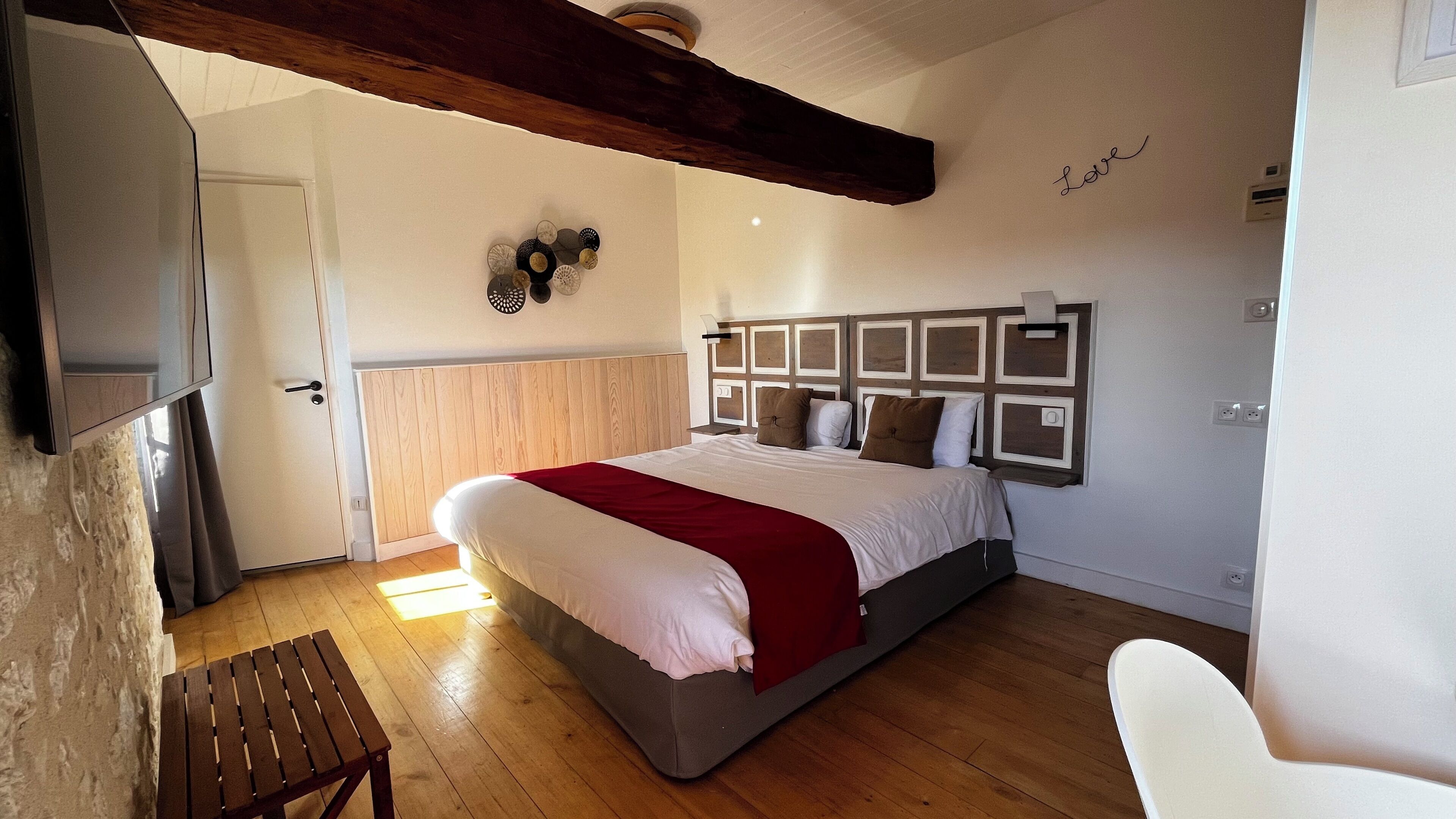 Ein Schlafzimmer mit Holzboden, einem Bett mit weiß-roter Bettdecke, einem hölzernen Kopfteil und einer Wand mit der Aufschrift 'Love'.