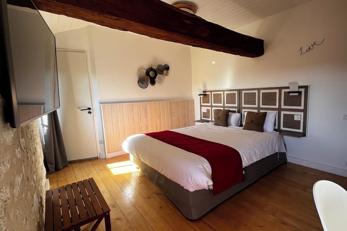 Un dormitorio con piso de madera, una cama con cubrecama blanco y rojo, cabecera de madera y una pared con el letrero 'Love'.
