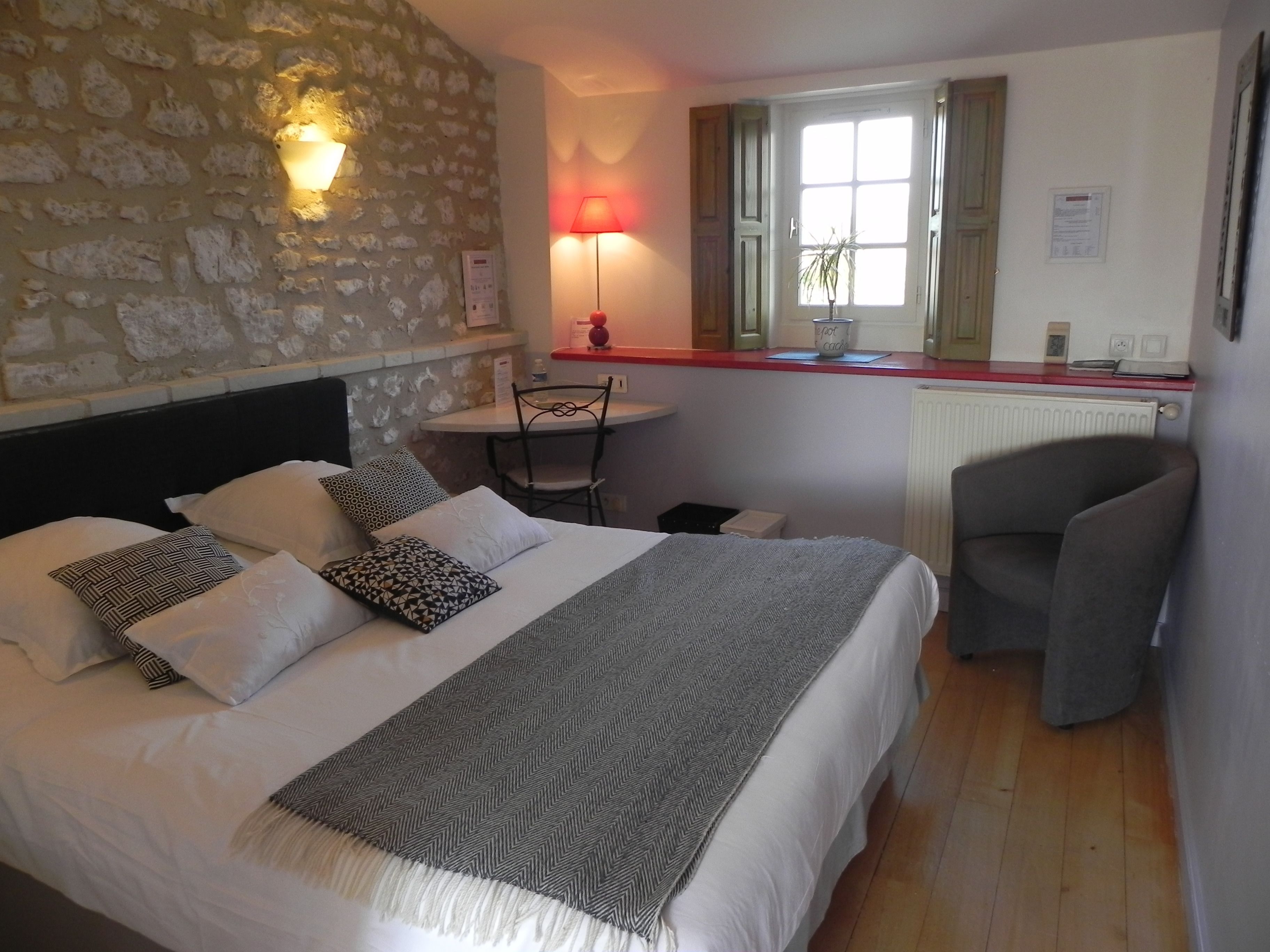 Une chambre avec un mur en pierre, un lit agrémenté d’oreillers à motifs, une table de chevet avec une lampe, une chaise et une fenêtre donnant sur un beau paysage.