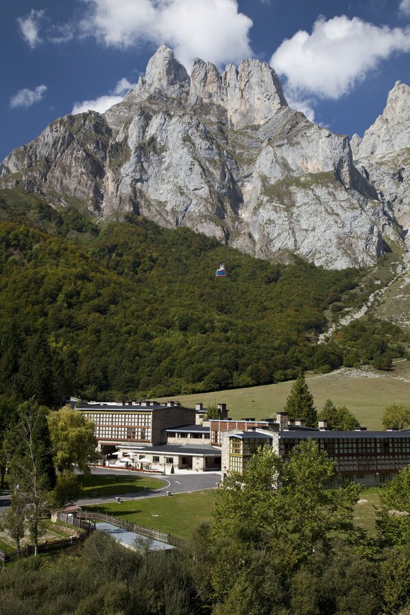 A modern building with a flat roof and a large glass facade, surrounded by lush greenery and mountains in the background.