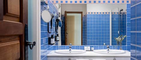 A bathroom with blue tiles, two sinks, a mirror, and a shower.