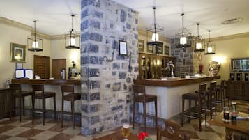 A bar area with stone walls, wooden bar stools, and hanging light fixtures.