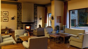 A cozy living room with a fireplace, comfortable seating, and a view through a large window.