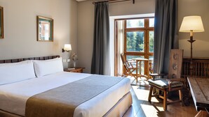 A hotel room with a large bed, a desk with a lamp, a chair, and a window with curtains.