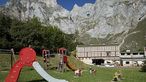 A playground with swings and slides, a building with a large window, and a mountain in the background.