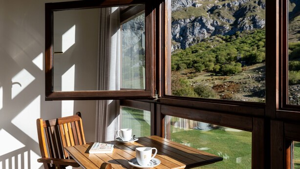 A wooden table with a chair and a window with a view of a mountainous landscape.