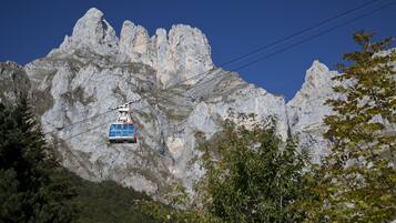 Un teleférico avanza sobre un cable con montañas agrestes al fondo.