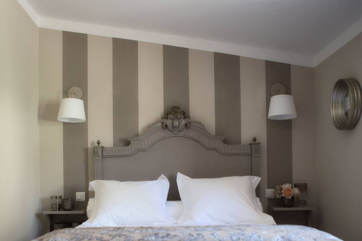 Un lit bien fait, avec du linge de lit blanc, un banc à rayures et une horloge murale.