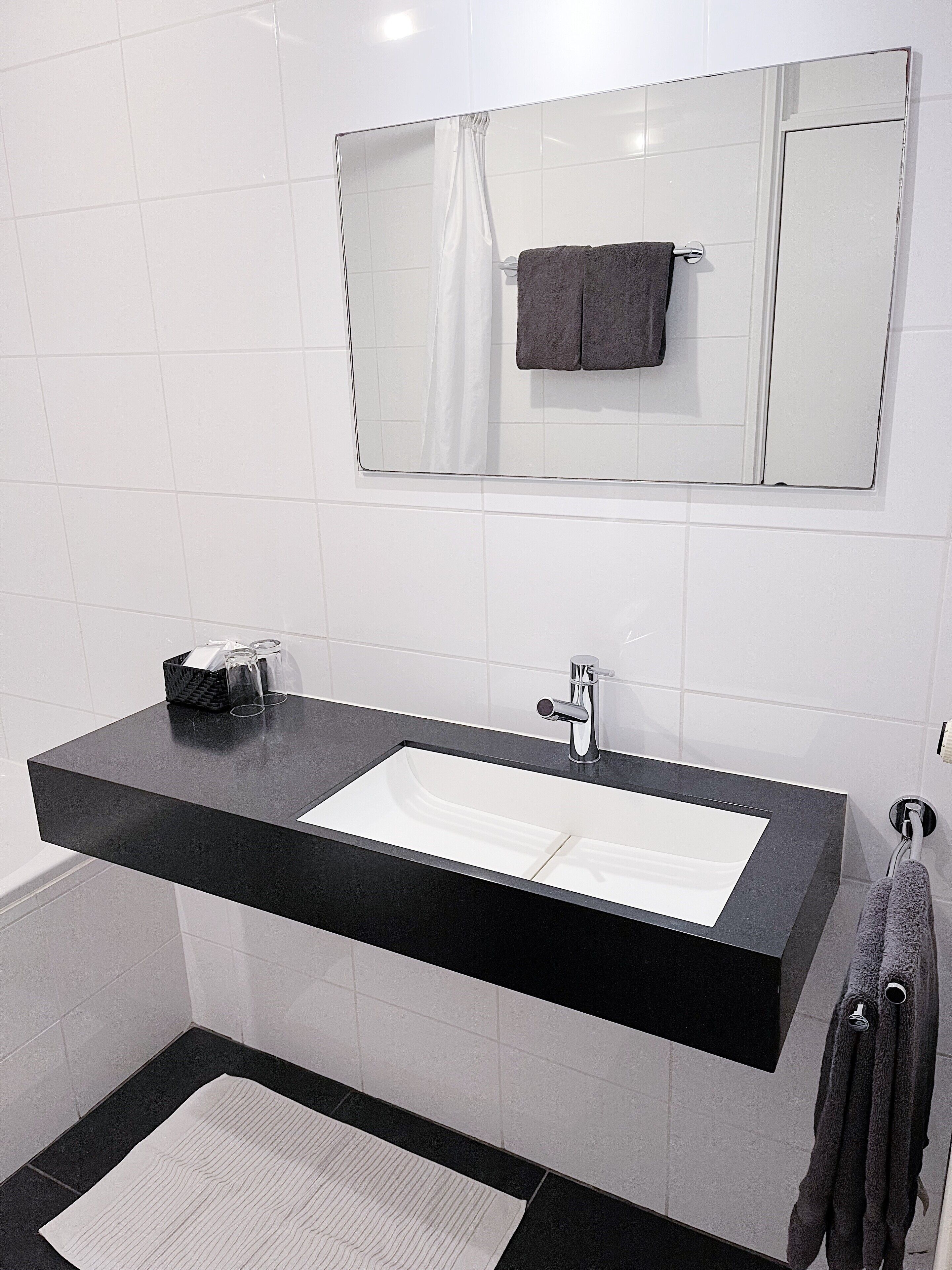 Un baño moderno con lavamanos de encimera negra, un espejo arriba y un perchero con dos toallas.
