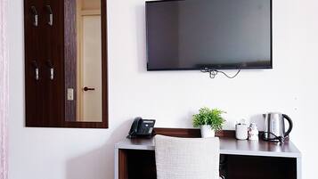 Habitación de hotel con cama, escritorio con silla, televisor, teléfono, hervidor y una planta en maceta.