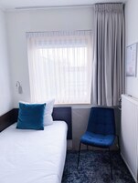 Habitación de hotel con cama, una silla, ventana con cortinas y radiador.