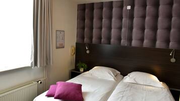 A hotel room with a large bed, a headboard, a bedside table with a lamp, and a window with curtains.