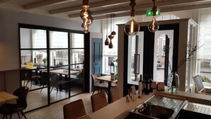 A modern restaurant interior with large windows, a bar area, and hanging pendant lights. - De Magneet (Hoorn)