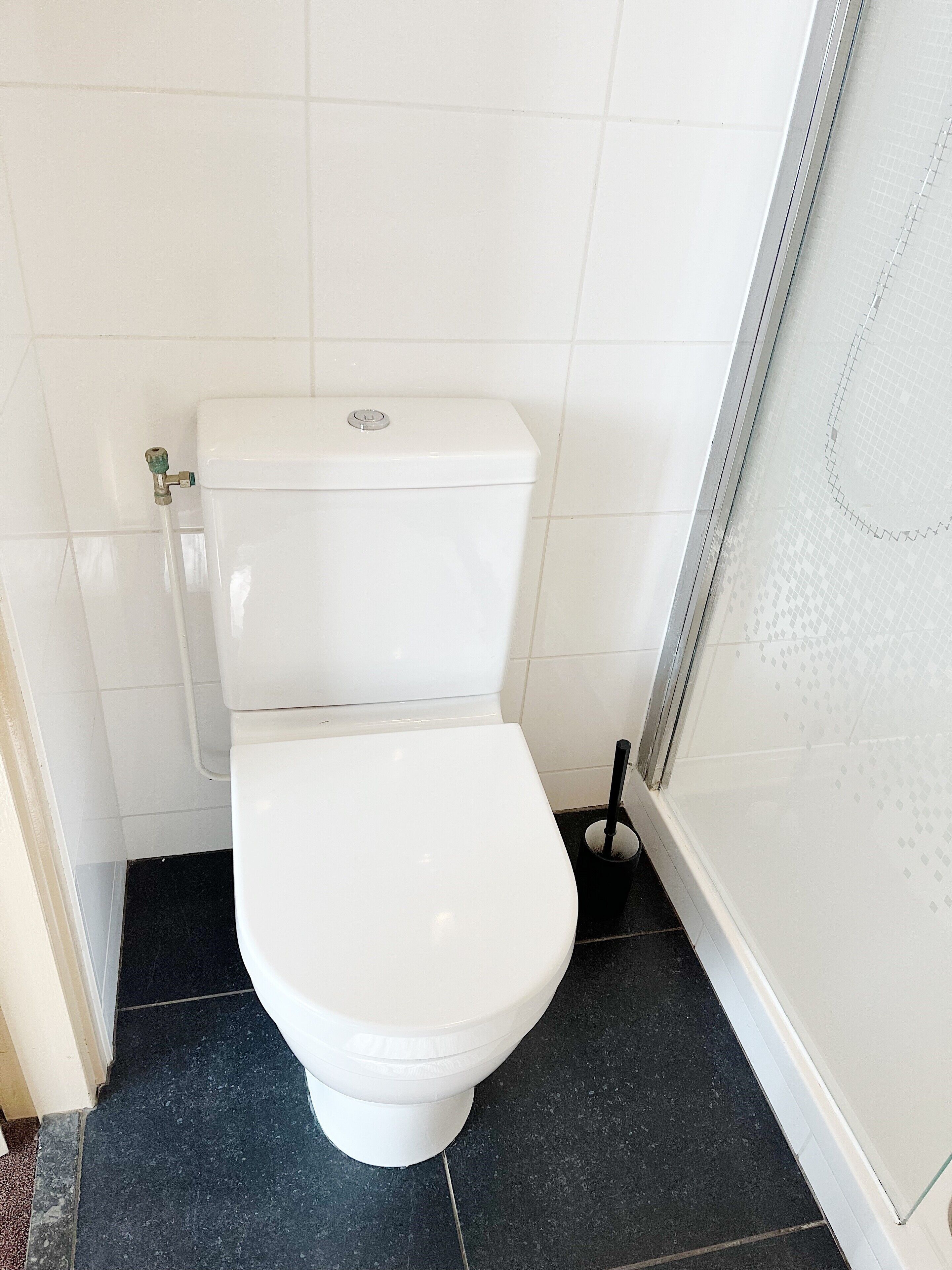 A white toilet with a tank and seat, a black floor, and a shower area with a glass door.