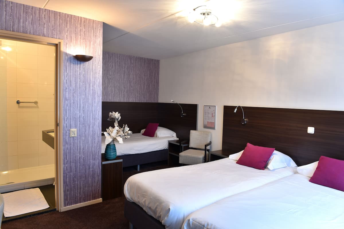A hotel room with two beds, a shower, a chair, and a small table with a vase of flowers.