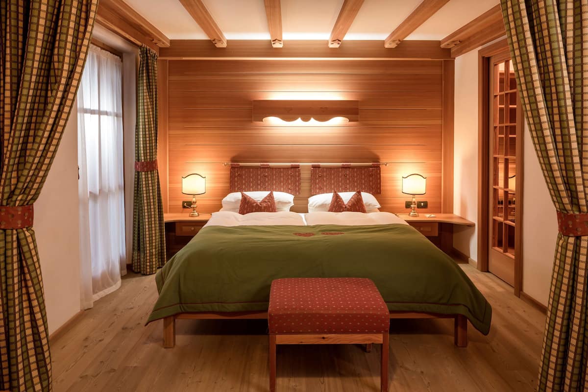 A room with a large bed, two bedside tables with lamps, a bench, and wooden paneling on the walls.
