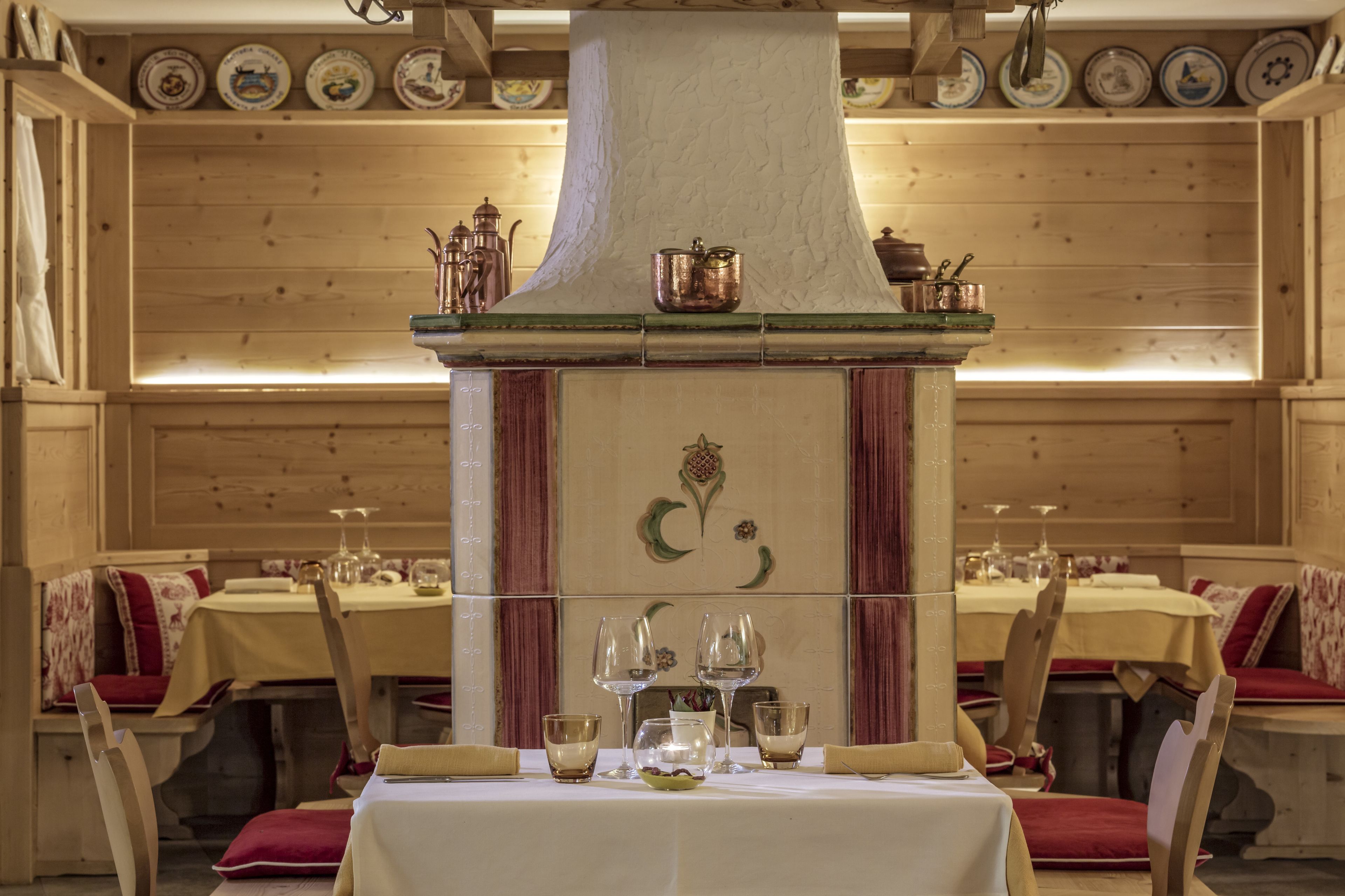 Un espace repas aux murs en bois et doté d’une cheminée centrale. Les tables sont dressées avec des nappes blanches et des coussins rouges.