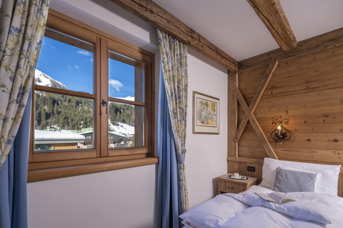 A bedroom with a wooden ceiling, a bed with white bedding, a nightstand with a lamp, and a window with curtains.