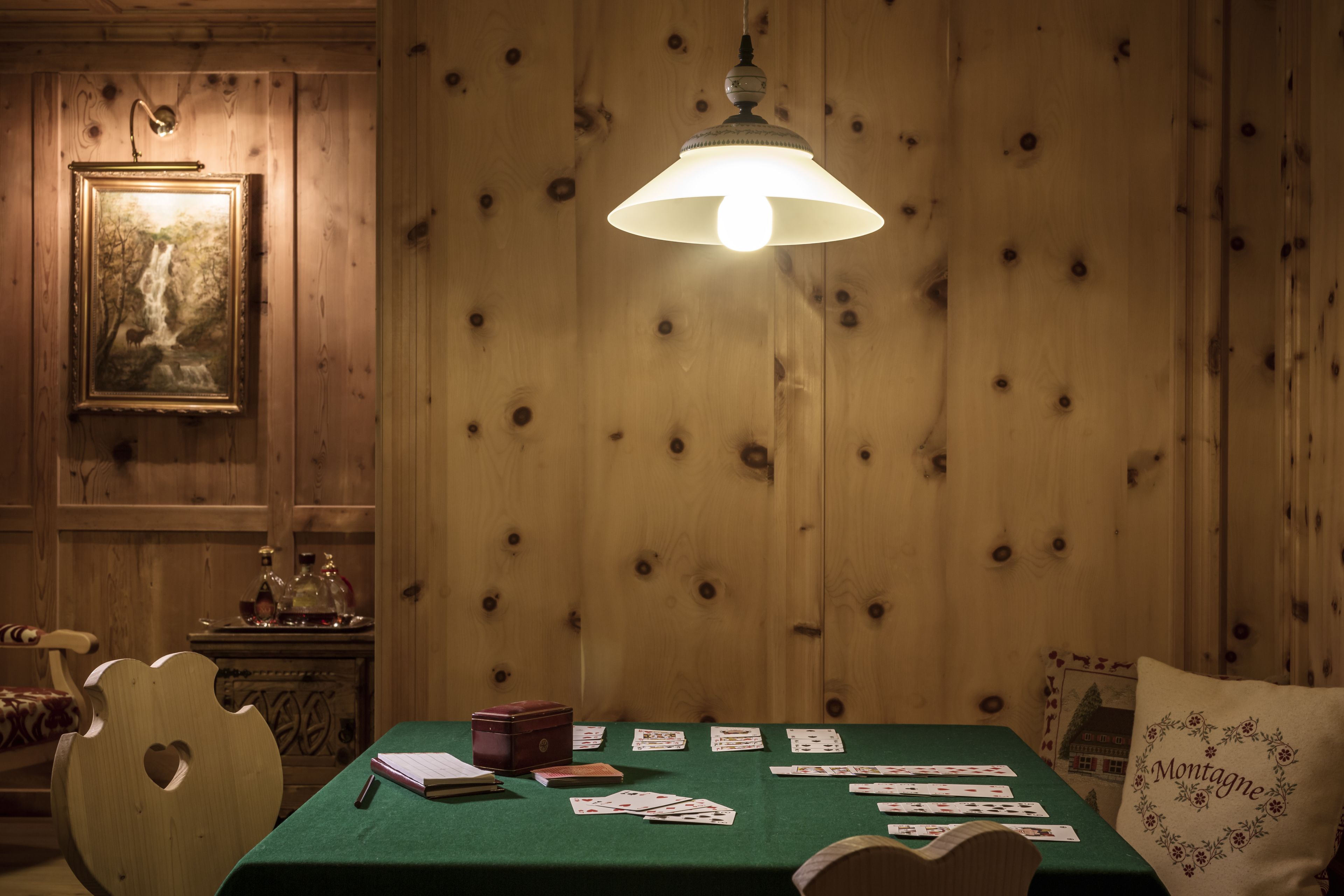 Una stanza con rivestimento in legno, un tavolo verde, carte da gioco e una lampada a sospensione.