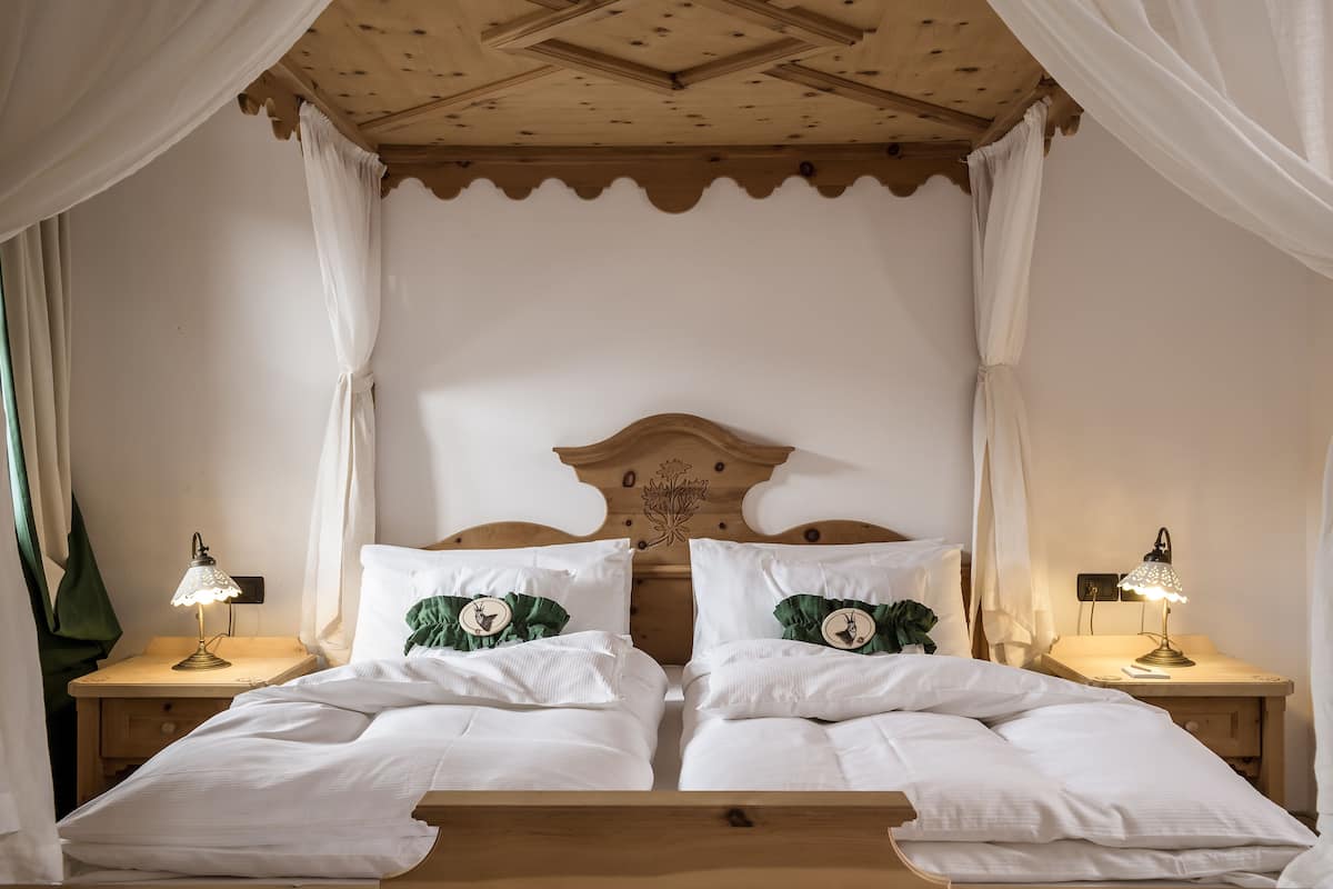 A double bed with a wooden headboard, two bedside tables with lamps, and white curtains.