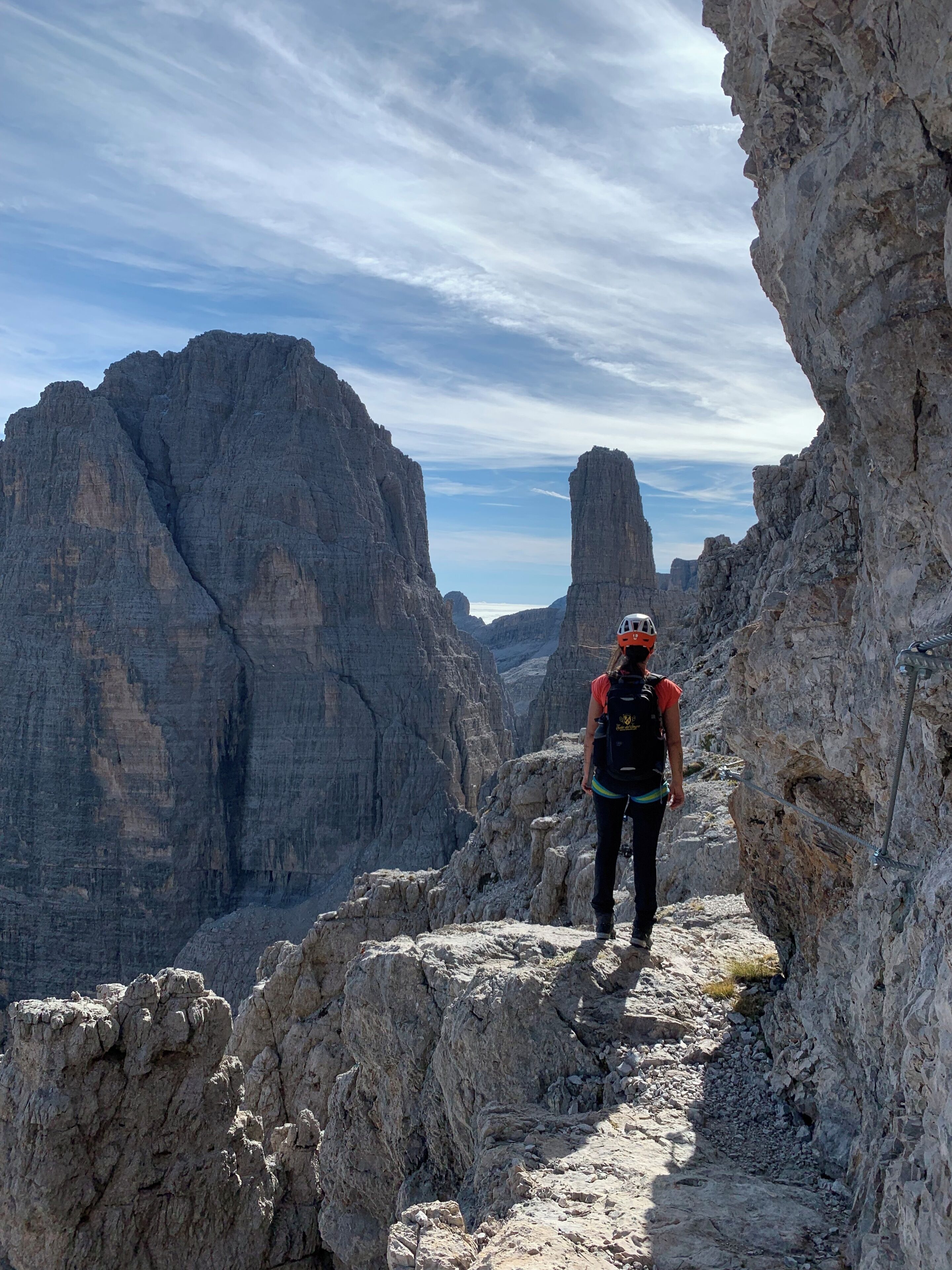 A hiker on a rocky trail with steep cliffs and a clear sky.