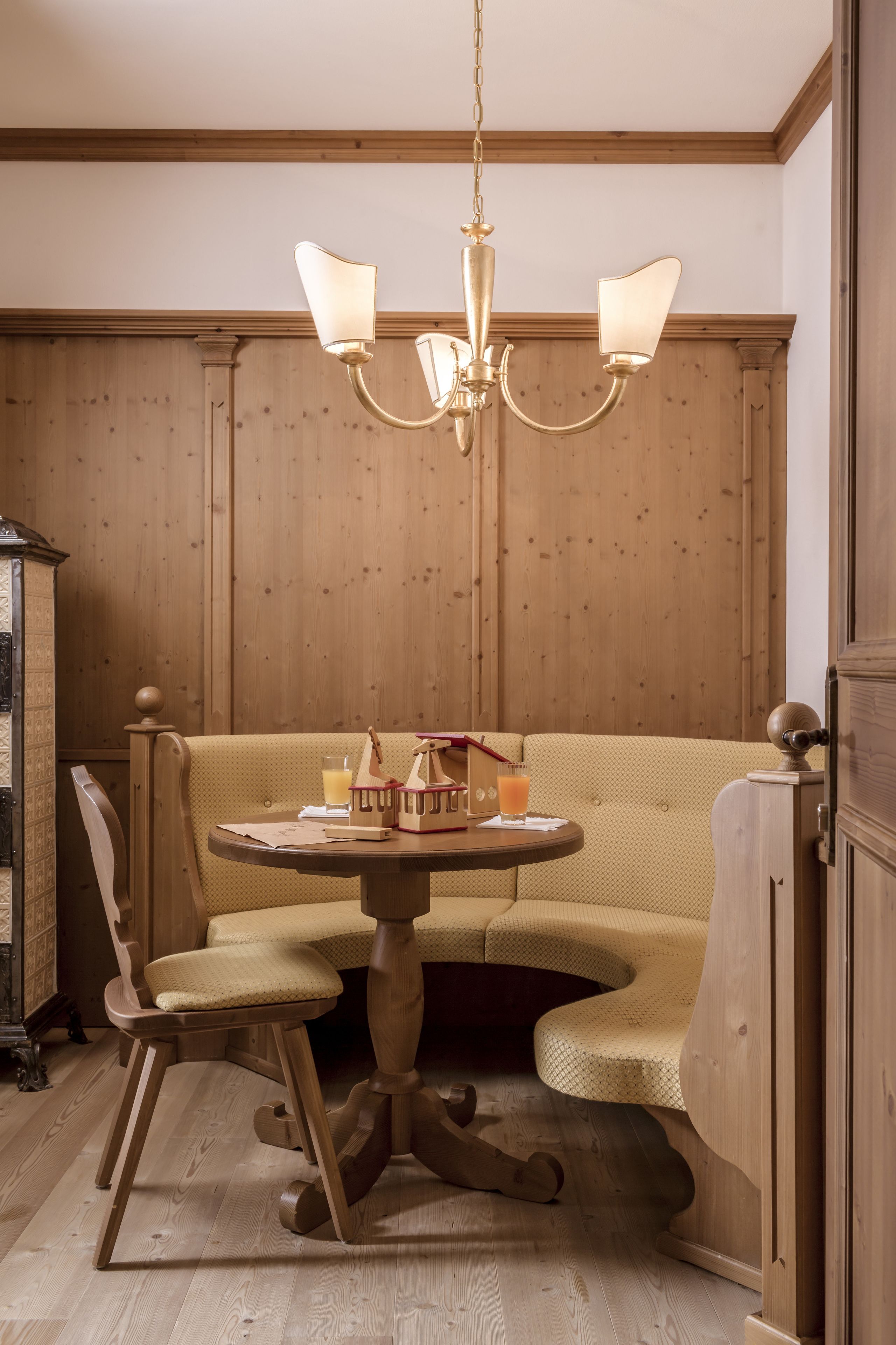 Une pièce aux murs lambrissés, avec une table ronde, un banc rembourré et un lustre.
