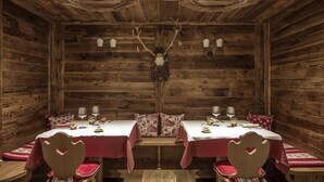 A rustic wooden dining room with a central elk skull, two tables with red tablecloths, and wooden chairs with heart-shaped cutouts. - Hotel Chalet del Sogno (Pinzolo)