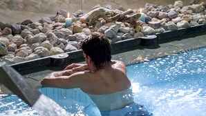 A person in a hot tub with water flowing into it, surrounded by rocks and candles. - Hotel Chalet del Sogno (Pinzolo)