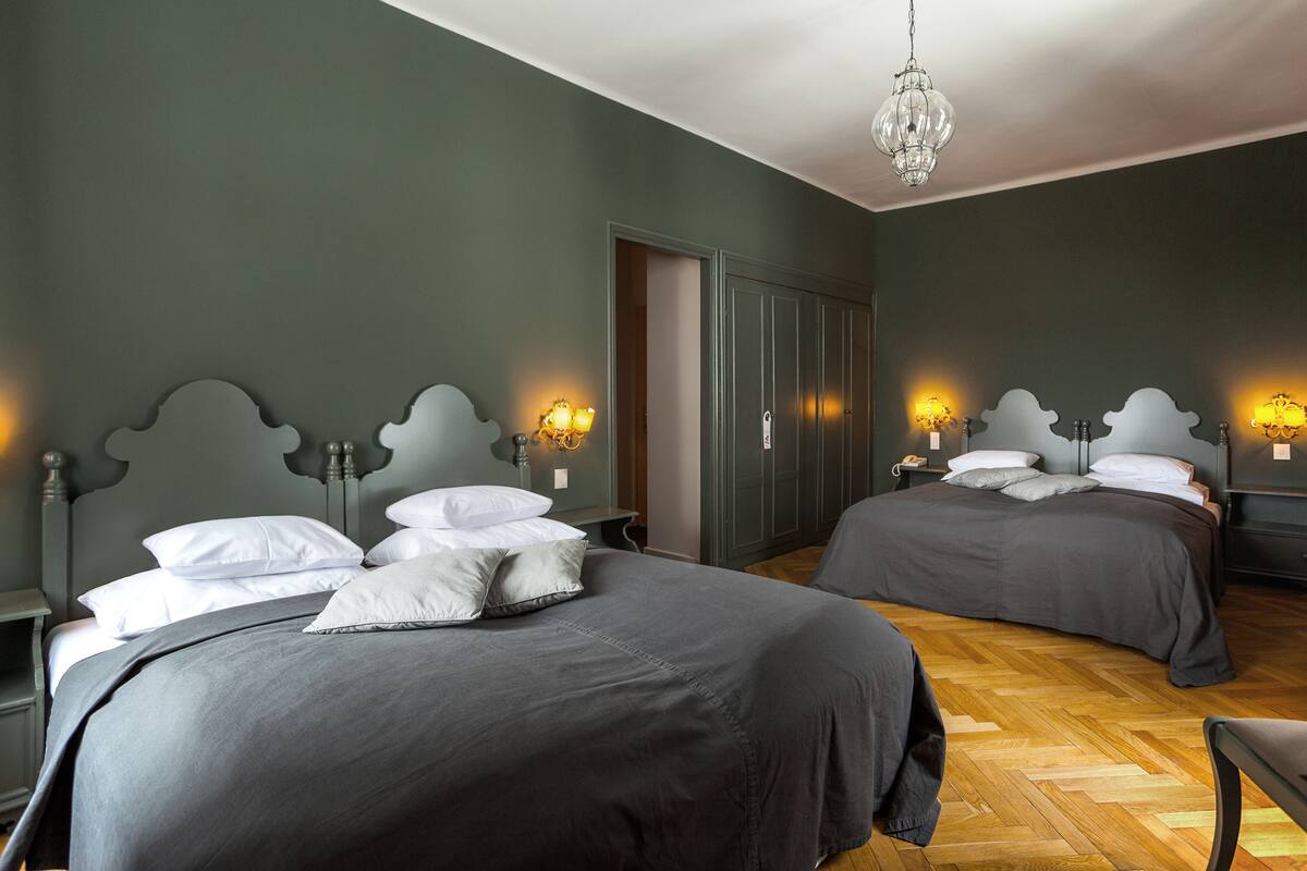 A bedroom with two beds, wooden flooring, and a chandelier.