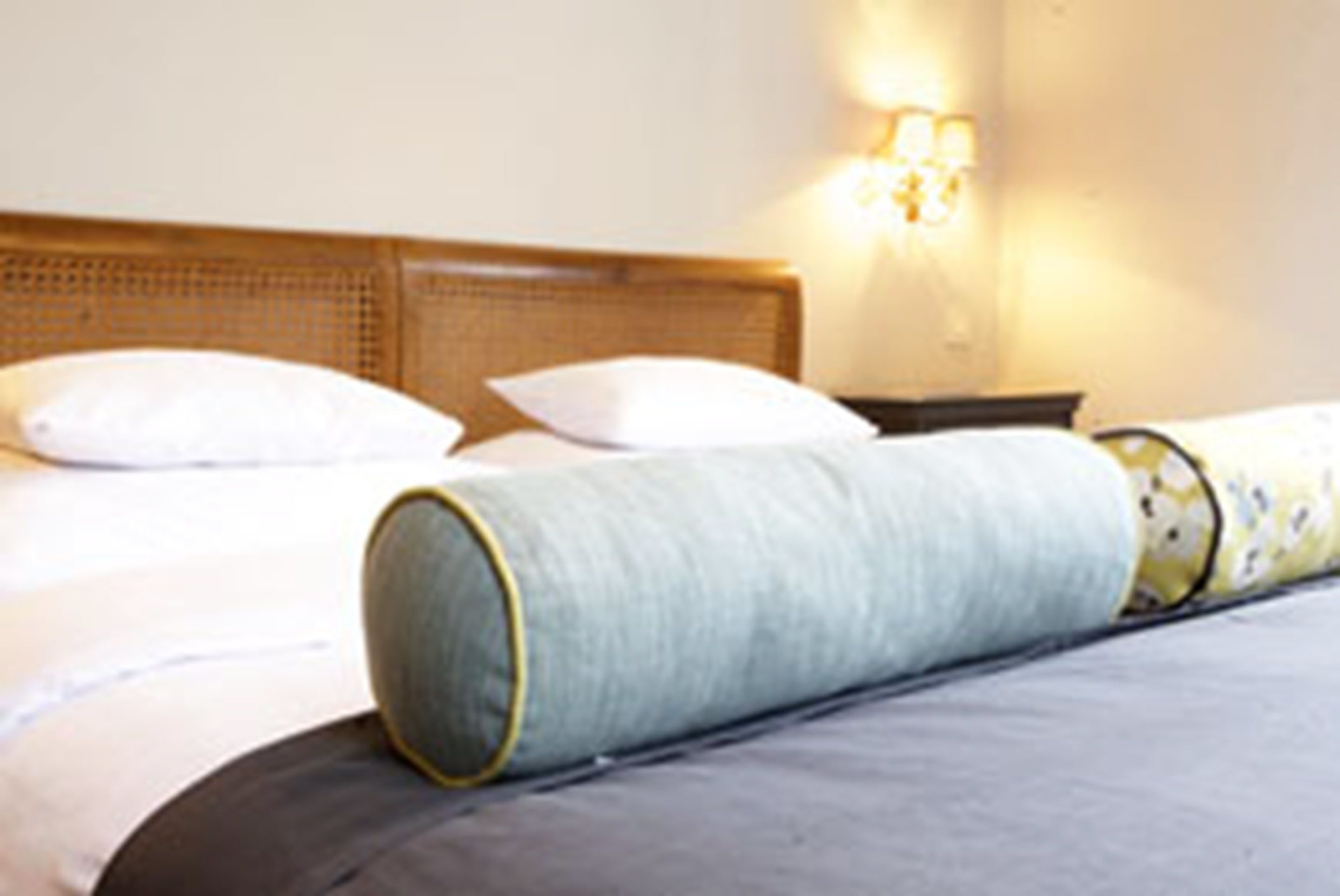 A neatly made bed with white pillows and a grey blanket, a wooden headboard, and a wall-mounted light fixture.