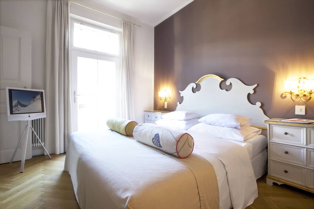 A hotel room with a large bed, bedside tables, a TV on a stand, and a window with curtains.