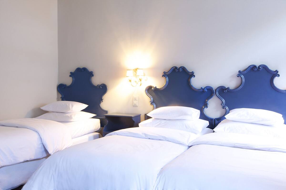 A hotel room with two beds, a nightstand with a lamp, and a wall-mounted light fixture.