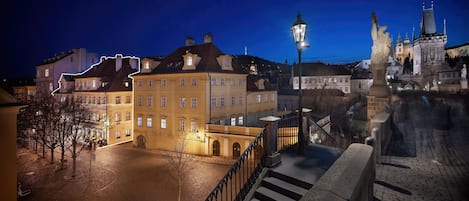 A historic building with a courtyard, a statue, and a bridge in the background.