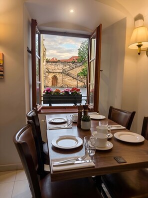 A dining area with a table set for four, a window with an open view of a stone bridge, and a potted plant with flowers on the windowsill. - Hotel At the Golden Scissors (Prague)
