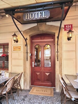 A hotel entrance with a red door, a sign above indicating 'HOTEL,' and a number sign '494' on the wall. - Hotel At the Golden Scissors (Prague)
