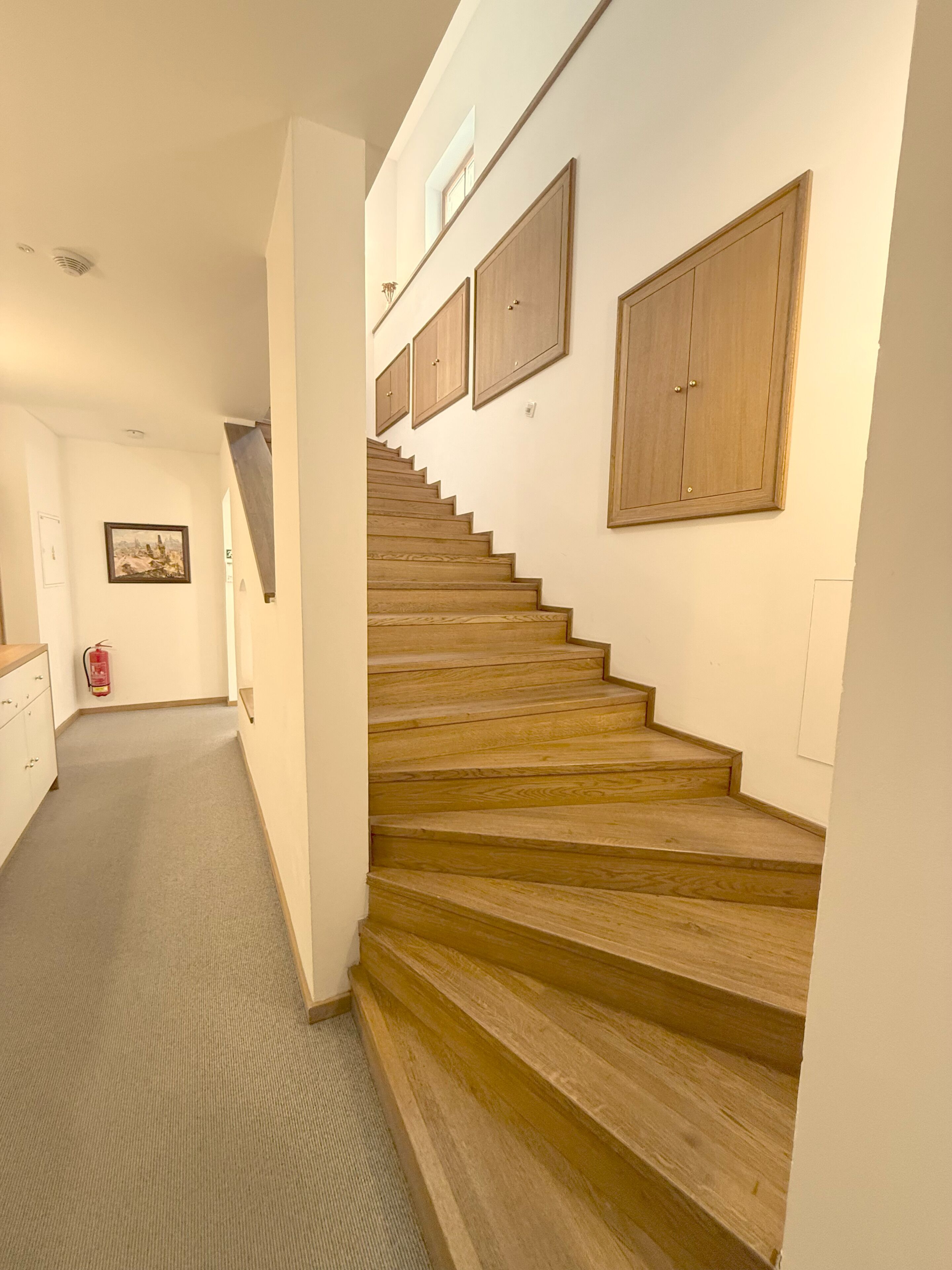 Una escalera con escalones de madera que conduce a una plataforma, un extintor en el suelo y un cuadro en la pared.