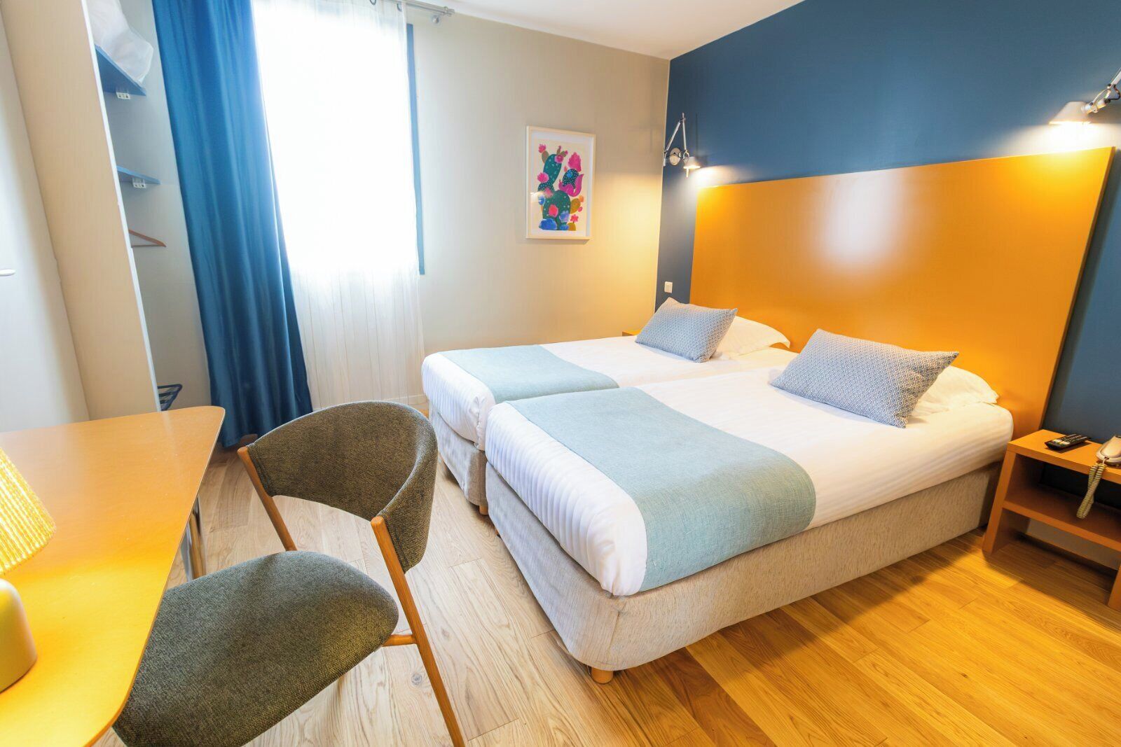 A hotel room with two beds, a desk, a chair, and a nightstand with a phone.