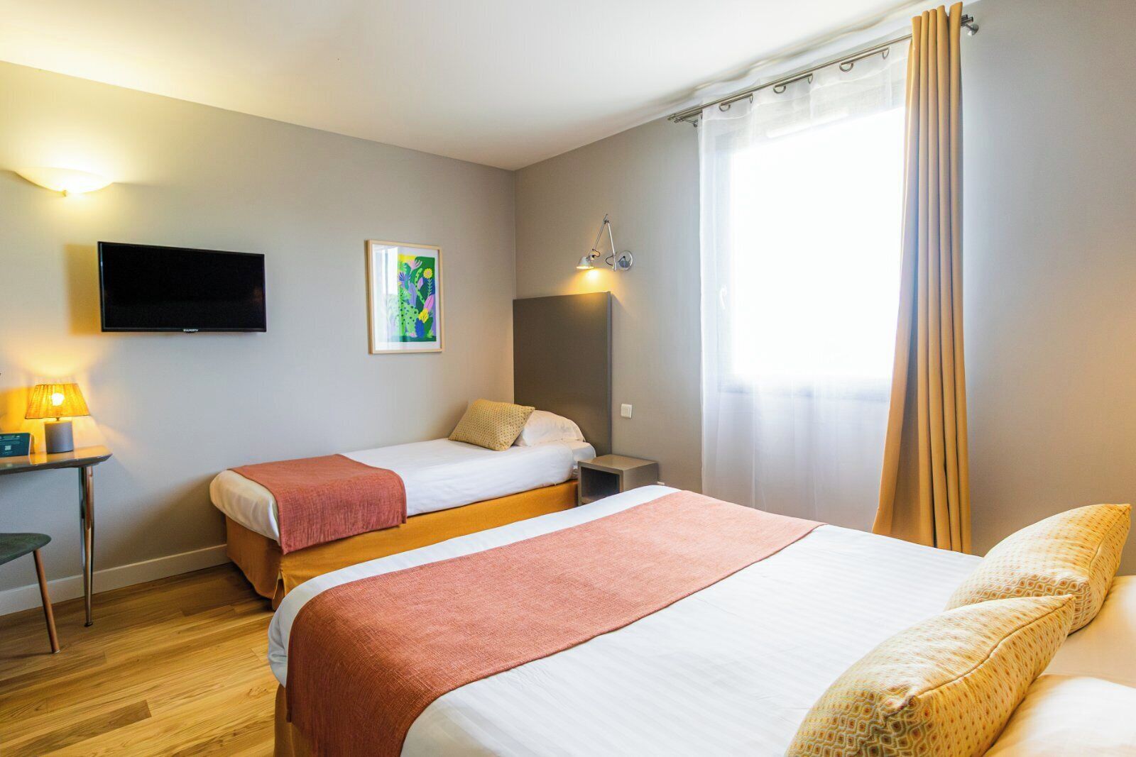 A hotel room with two beds, a TV, a bedside table with a lamp, and a painting on the wall.