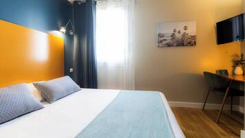 A hotel room with a bed, a desk, a chair, a TV, and a painting on the wall.