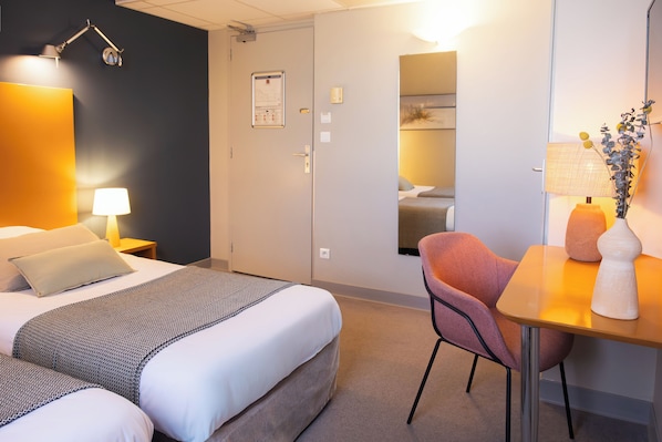 Habitación de hotel con cama, mesita de noche, lámpara, silla y una pequeña mesa con un florero.