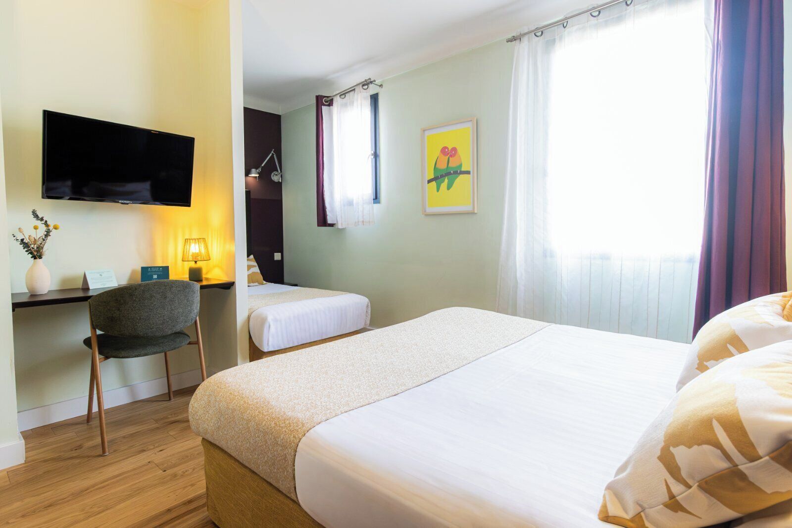 A hotel room with two beds, a desk with a chair, a flat-screen TV, a lamp, and a window with curtains.